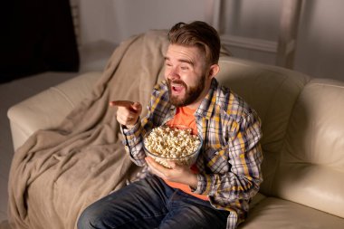 Kanepede oturup televizyon izleyen ve patlamış mısır yiyen genç adamın portresi.