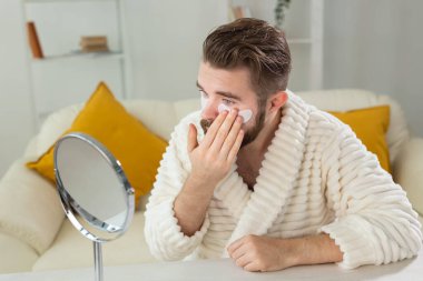Sakallı adam yüzüne göz bandı yapıştırıyor. Erkekler için kırışıklıklar ve yüz bakımı.