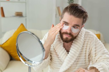 Sakallı adam yüzüne göz bandı yapıştırıyor. Erkekler için kırışıklıklar ve yüz bakımı.