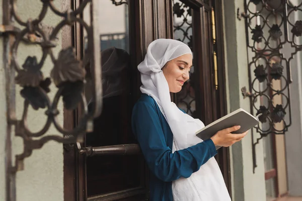 Retrato de jovem muçulmana usando hijab leitura livro ao ar livre — Fotografia de Stock