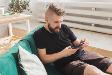 Evdeki oturma odasındaki yeşil koltukta oturan rahat adam akıllı telefon kullanıyor.