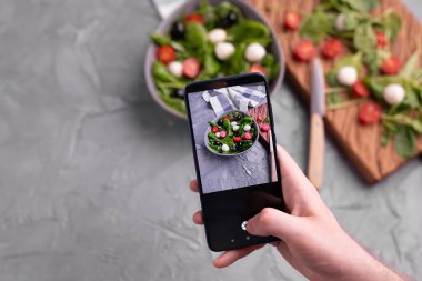 Mozarella ve cep telefonu kamerasında ıspanak ile taze sebze salatası çeken bir adam. Yemek pişirme, blog yazma ve sağlıklı beslenme kavramı.