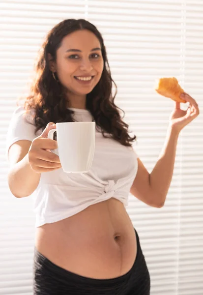 Счастливая беременная женщина с круассановыми булочками дома. Беременность, питание и концепция людей — стоковое фото