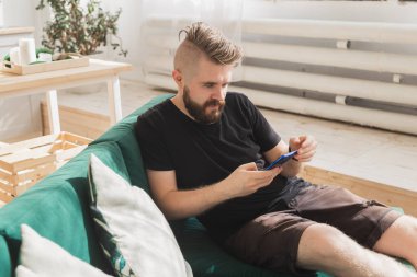 Evdeki oturma odasındaki yeşil koltukta oturan rahat adam akıllı telefon kullanıyor.