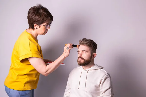 Artista de maquillaje profesional haciendo maquillaje de hombre joven en el estudio —  Fotos de Stock