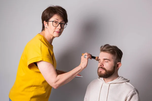 Artista de maquillaje profesional haciendo maquillaje de hombre joven en el estudio —  Fotos de Stock