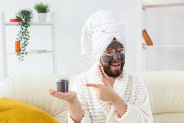 Yüzünde siyah kilden yapılmış kozmetik maskeyle eğlenen sakallı bir adam. Erkeklerin cilt bakımı, mizah ve spa konsepti