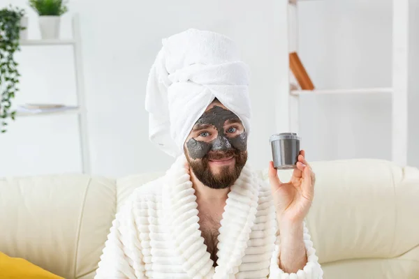 Hombre barbudo divirtiéndose con una máscara cosmética en su cara hecha de arcilla negra. Cuidado de la piel de los hombres, humor y spa en el hogar concepto —  Fotos de Stock