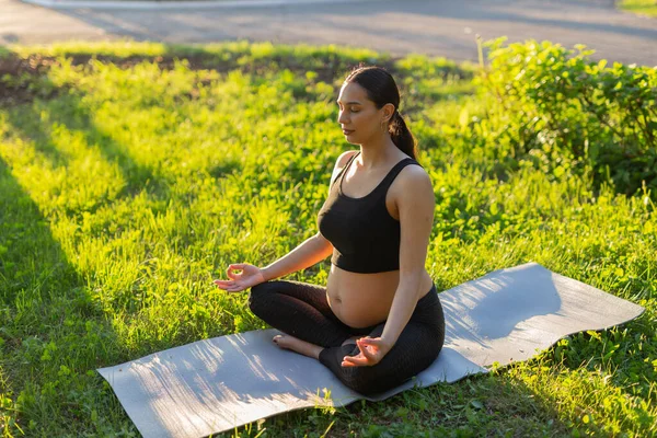 Ung gravid kvinna mediterar i naturen, utövar yoga. Vård av hälsa och graviditet — Stockfoto
