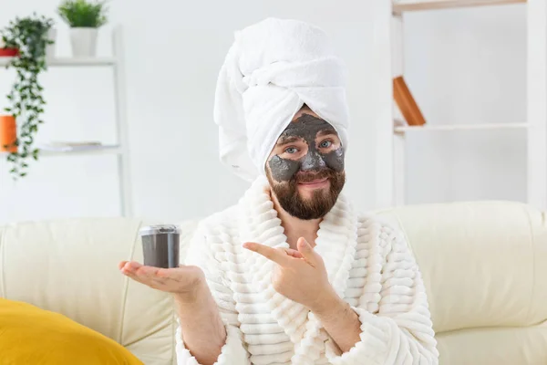 Бородач веселится с косметической маской на лице, сделанной из черной глины. Мужчины уход за кожей, юмор и спа на дому концепции — стоковое фото