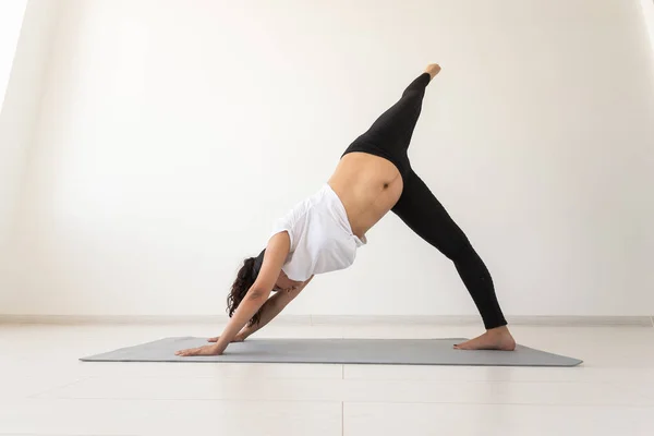 Joven mujer embarazada flexible haciendo gimnasia en la alfombra en el suelo sobre fondo blanco. El concepto de preparar el cuerpo para el parto fácil. Copiar espacio. —  Fotos de Stock