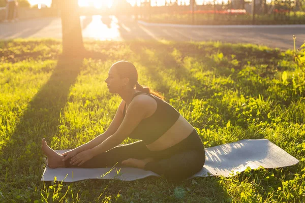 Lugn ung positiv gravid kvinna i gymnastik kostym gör yoga och meditera sitter på matta på grönt gräs på solig varm sommardag. Begreppet förberedelse för förlossning och positiv inställning — Stockfoto