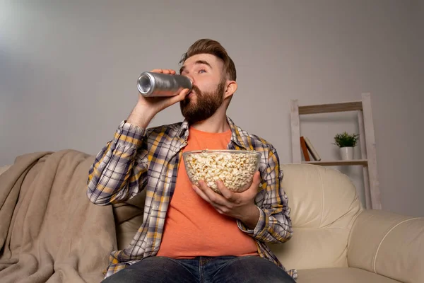 Vousáč, který se dívá na film nebo sportovní hry, jí popcorn a v noci pije pivo v domě. Kino, mistrovství a fanouškovský koncept. — Stock fotografie