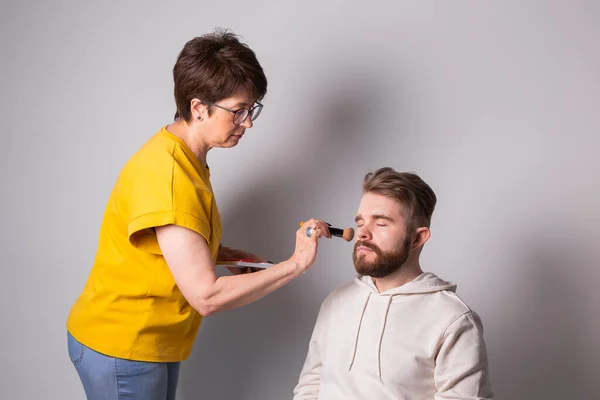 Hombre barbudo maquillándose. Mujer visagista trabaja con cepillo. —  Fotos de Stock