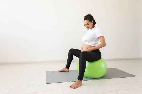 Una joven embarazada haciendo ejercicio de relajación usando una pelota de fitness mientras está sentada en una esterilla. Espacio de copia. —  Fotos de Stock