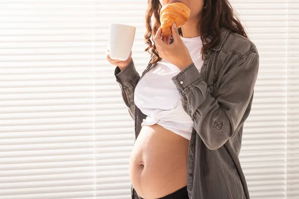 Mulher grávida bonita saudável beber chá e comer croissant durante o almoço. Conceito de nutrição de alta caloria enquanto espera pelo nascimento do bebê. Espaço de cópia. — Fotografia de Stock