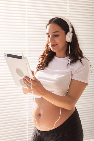 Беременная женщина слушает музыку в наушниках с цифровым планшетом — стоковое фото