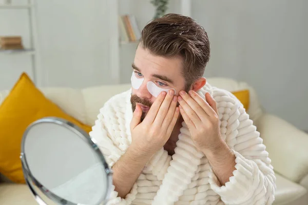 Bearded man applying eye patches on his face. Wrinkles and face home care for men. — Stock Photo, Image