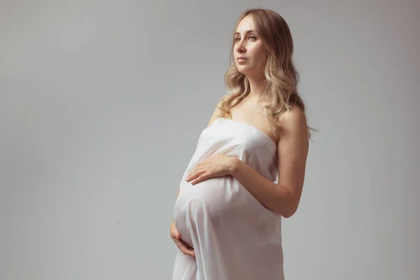 Mujer joven embarazada elegante de pie usando tela ligera. Concepto de embarazo, fantasía y cuento de hadas. — Foto de Stock