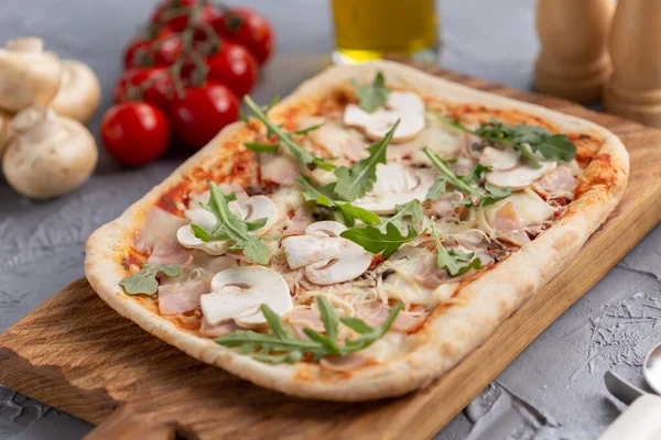 Прямоугольная пицца с грибами, помидорами и рукколой на деревянной доске — стоковое фото