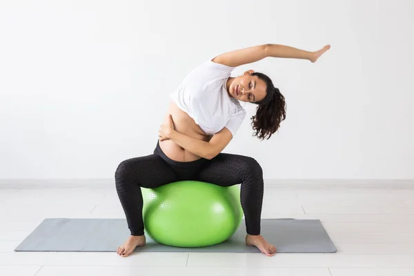 Una joven embarazada haciendo ejercicio usando una pelota de fitness mientras está sentada en una alfombra. —  Fotos de Stock