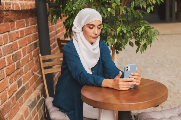 Happy muslim woman having video call on smartphone in street cafe — Stock Photo, Image