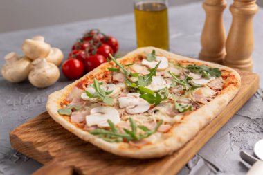 Mantarlı, domatesli ve roka kaplı dikdörtgen pizza.