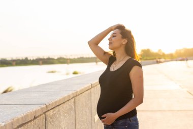Gün batımında parkta yürüyen mutlu ve hamile bir Latin kadının portresi. Hamilelik ve annelik kavramı.