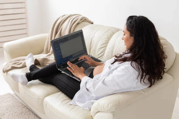 Latynoska kobieta w ciąży używająca laptopa siedzącego na kanapie w domu. Ciąża i informacje dotyczące koncepcji rodzicielstwa. — Zdjęcie stockowe