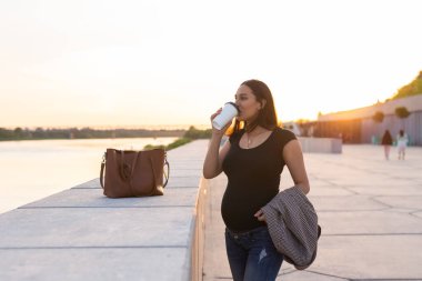 Hispanic pregnant woman drinking take away coffee outdoors. Copy space.