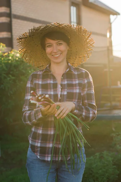 Радостная женщина садовница нюхает зеленый лук в солнечный теплый весенний день. Уход за растениями и сбор урожая и хобби — стоковое фото