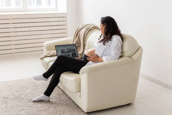 Terhes nő használja laptop, miközben ül a kanapén a nappaliban otthon — Stock Fotó