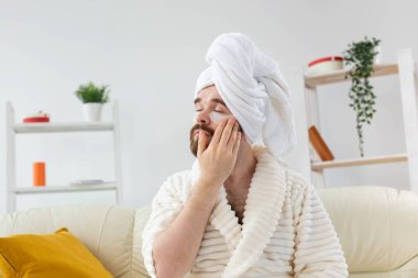 Sakallı adam yüzüne göz bandı yapıştırıyor. Erkekler için kırışıklıklar ve yüz bakımı.