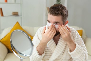 Sakallı adam yüzüne göz bandı yapıştırıyor. Erkekler için kırışıklıklar ve yüz bakımı.