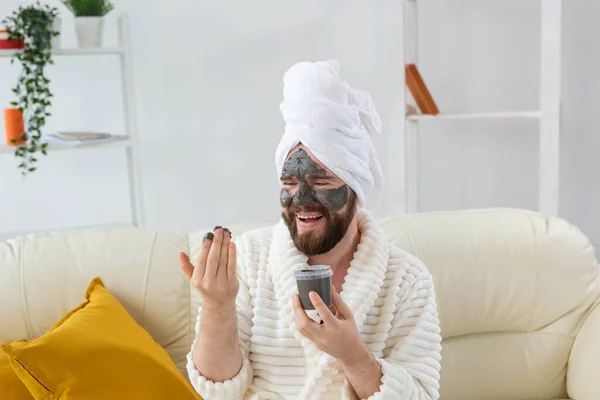 Αστείος γενειοφόρος που διασκεδάζει με μια πλαστική μάσκα στο πρόσωπό του φτιαγμένη από μαύρο πηλό. Άνδρες φροντίδα του δέρματος, χιούμορ και spa στο σπίτι έννοια — Φωτογραφία Αρχείου