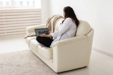 Latin hamile kadın evdeki koltukta dizüstü bilgisayar kullanıyor. Ebeveynlik kavramı için hamilelik ve bilgi.