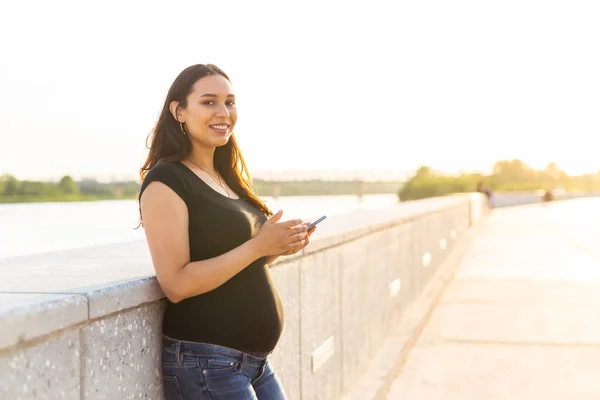 Gravid kvinna med smartphone utomhus. Graviditet, teknik och kommunikation — Stockfoto