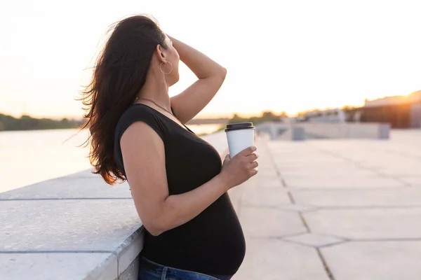 Pregnant woman with long hair holds smartphone outdoors. Side view with copy space. Warm day. New life, new horizons and opportunities concept — Stockfoto