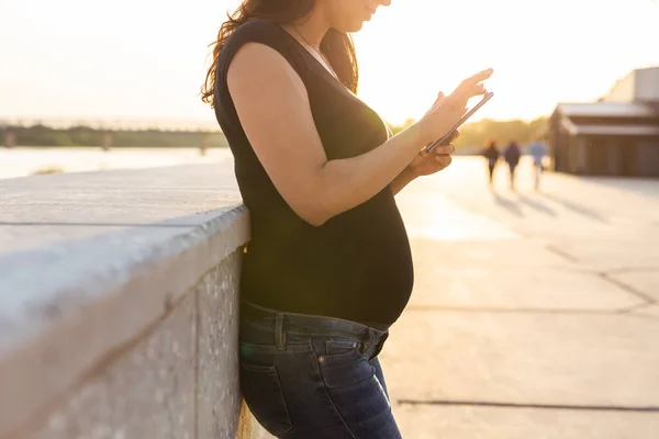 Närbild av gravida kvinna med smartphone i parken. Graviditet, teknik och kommunikation. — Stockfoto