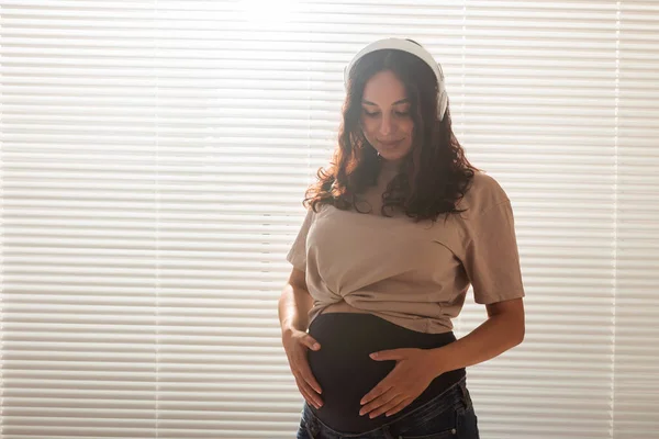 Lycklig gravid kvinna med lockigt hår lyssnar musik i hörlurar, kopiera utrymme. — Stockfoto