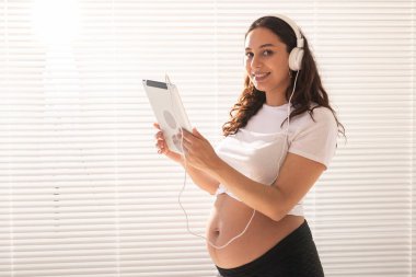 Dijital tablet kullanan İspanyol hamile kadın. Teknoloji, hamilelik ve annelik izni