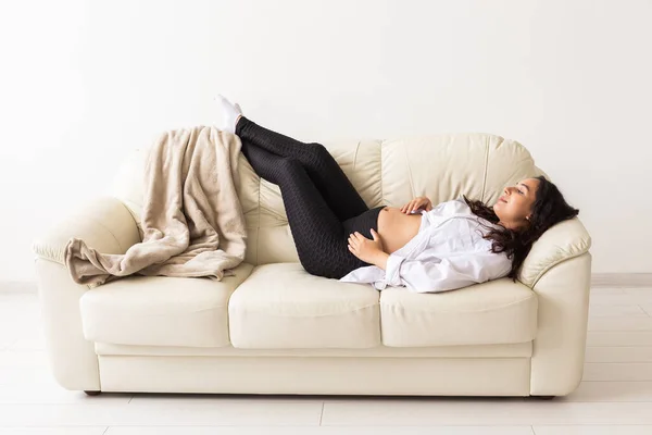 İspanyol hamile kadın evdeki kanepede yatıyor. Hamilelik, dinlenme ve beklenti konsepti. — Stok fotoğraf