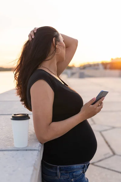 Gravid kvinna med långt hår håller smartphone utomhus. Sidovy. Varm dag. Nytt liv, nya horisonter och möjligheter — Stockfoto