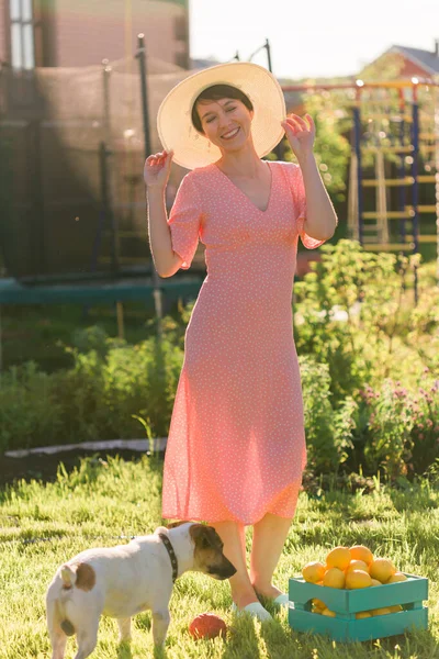 Meisje in een lange roze jurk staat in de tuin met haar jack russell terriër hond. Vrouw loopt met de hond. Huisdieren eigenaar en verantwoordelijke houding ten opzichte van dieren concept. — Stockfoto