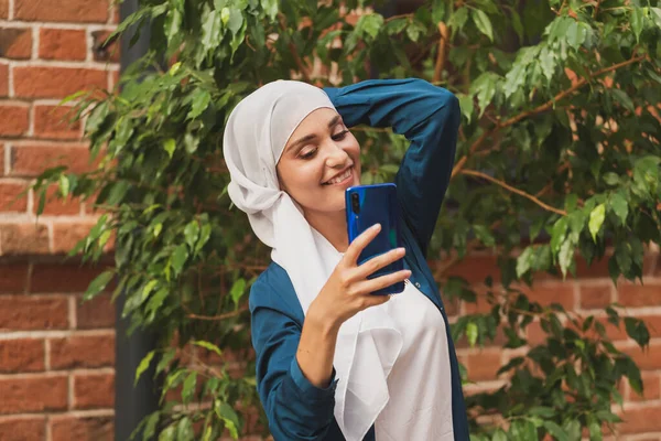 Müslüman kadın selfie çekiyor. Fularlı mutlu güzel kız akıllı telefon kullanarak kendi fotoğrafını çekiyor.. — Stok fotoğraf