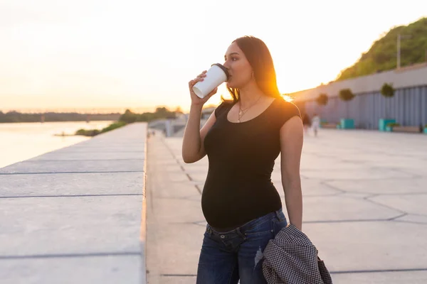 年轻的孕妇在堤岸上喝外卖咖啡或茶。产妇、休闲和健康概念。广告区工作空间 — 图库照片