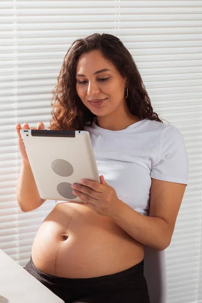 Mujer embarazada hispana usando tableta digital durante el desayuno. Tecnología, embarazo y permiso de maternidad —  Fotos de Stock