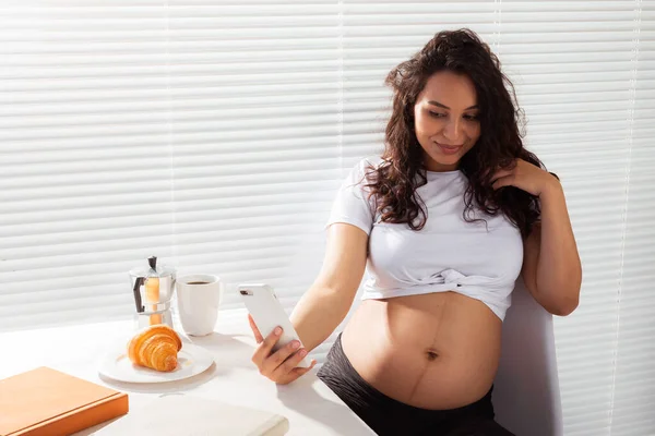 Donna incinta che scatta un autoritratto con il suo smartphone mentre fa colazione — Foto Stock