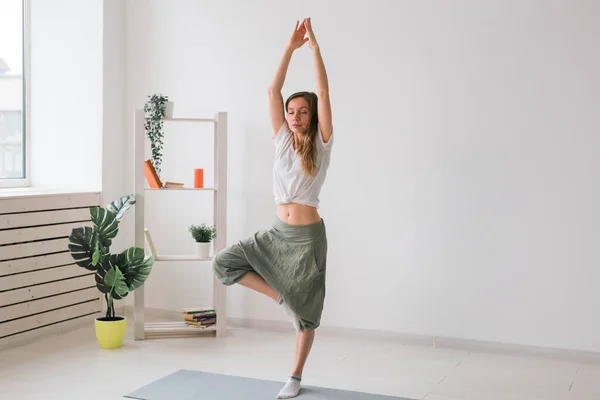 La mujer practica yoga. Árbol pose de pie en la estera en el interior de la habitación acogedora con plantas y vegetación. Concepto de estilo de vida saludable. Copiar espacio. — Foto de Stock