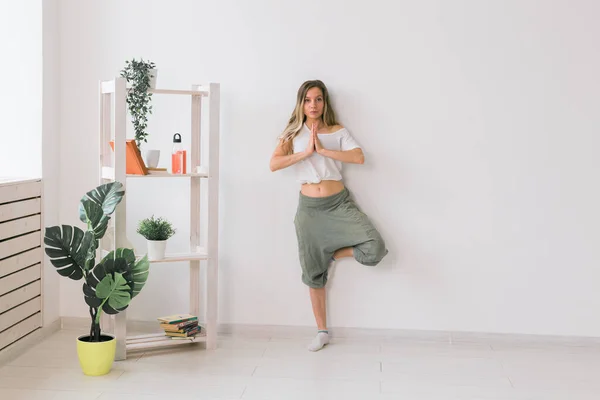 La mujer practica yoga. Árbol pose de pie en la estera en el interior de la habitación acogedora con plantas y vegetación. concepto de estilo de vida saludable — Foto de Stock